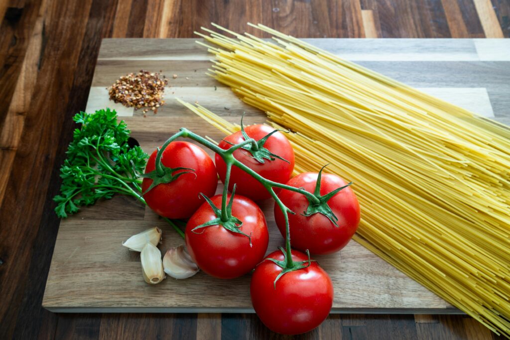 A vibrant still life of fresh tomatoes, parsley, garlic, and spaghetti on a wooden surface.